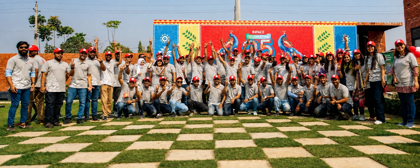 Inpace team celebrating its 25th anniversary in front of a colorful mural.